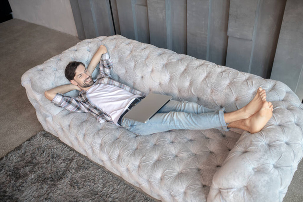 Young man with a laptop lying on a sofa. - Fotografie, Obrázek
