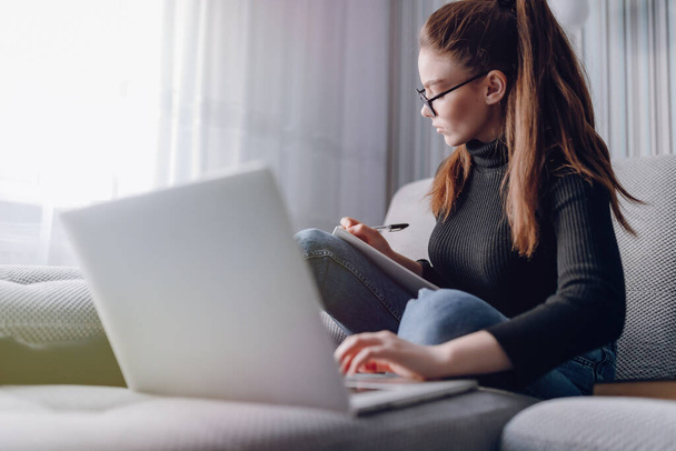 cozy young attractive girl at home working with laptop on the couch. comfort and coziness while at home. home office and work from home. remote online employment. - Fotografie, Obrázek