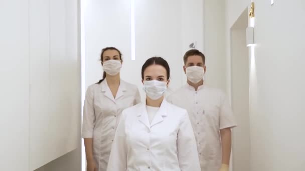 Three masked doctors walk down the corridor of a modern hospital in slow motion - Séquence, vidéo