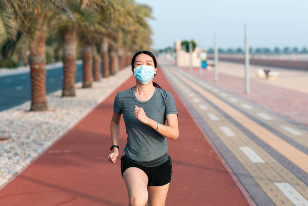 Asian woman jogging on the running track wearing protective surgical mask to prevent coronavirus spreading and stay safe - Foto, imagen