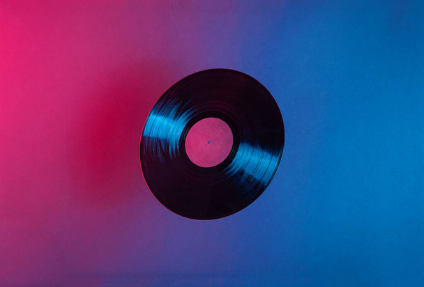 LP disco de vinilo iluminado con luz de neón de color azul y rojo. Espacio para texto. Concepto futurista de música vintage
. - Foto, Imagen