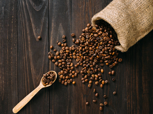 Spilling coffee beans on dark wooden table flat lay. Traditional concept. - Photo, Image
