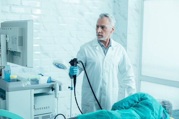 Serious mature doctor holding a modern endoscope and preparing for the procedure - Valokuva, kuva