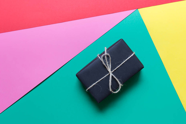 Colorful gift card with a present wrapped in black paper with rough packthread bow on green yellow pink and red paper background. - Фото, зображення
