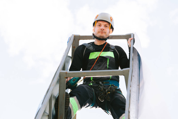 Portrait of Industrial climber in helmet and overall working on height. Risky job. Bottom view - Photo, image