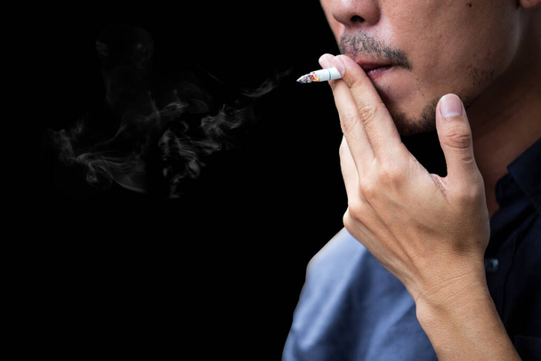 Boční pohled na mladý vousatý muž kouření cigarety na černém pozadí. - Fotografie, Obrázek