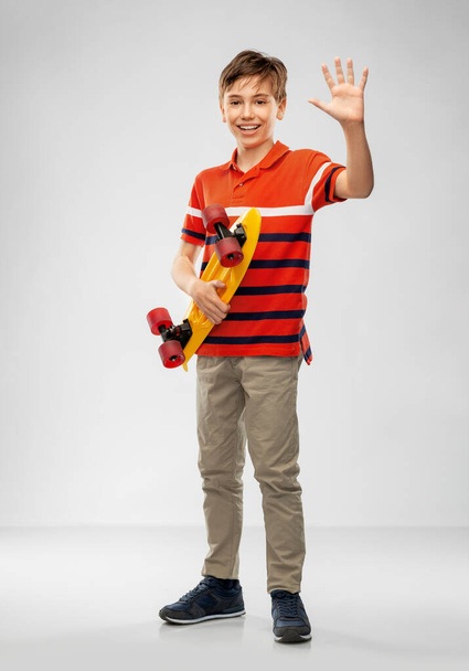 smiling boy with short skateboard waving hand - 写真・画像