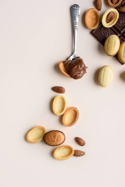 A bar of chocolate lies on a light background with almonds, walnuts, nuts with boiled condensed milk. View from above, place for text. Flat lay - Photo, Image