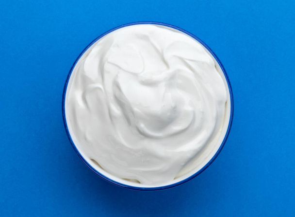 Bowl of sour cream on blue background, top view, flat lay - Fotoğraf, Görsel