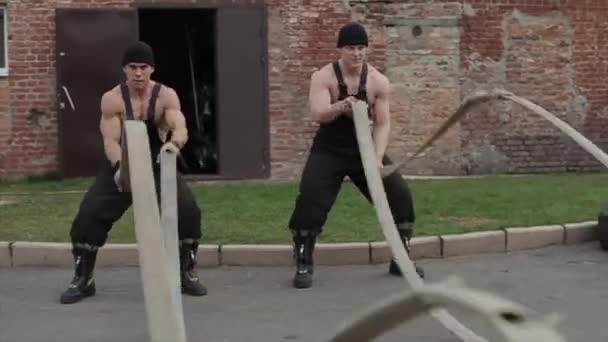 Δύο νέοι μυώδεις άνδρες εκπαίδευση και να κάνει ασκήσεις crossfit με σχοινιά μάχης. Η κάμερα ζουμάρει από κοντά. - Πλάνα, βίντεο