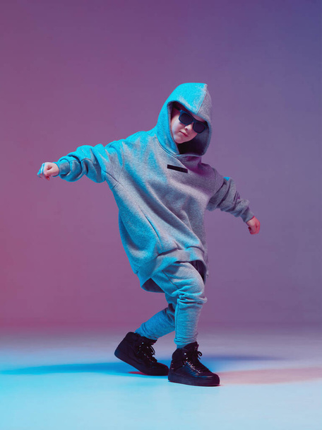 Cool boy child dancing hip hop in a hoodie and glasses, in a Studio on a neon background. - Photo, image