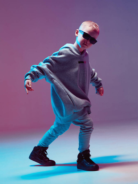 Cool boy child dancing hip hop in a hoodie and glasses, in a Studio on a neon background. - Fotografie, Obrázek