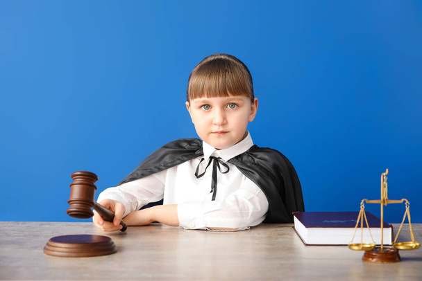 Portrait of little judge sitting at table against color background - Photo, Image