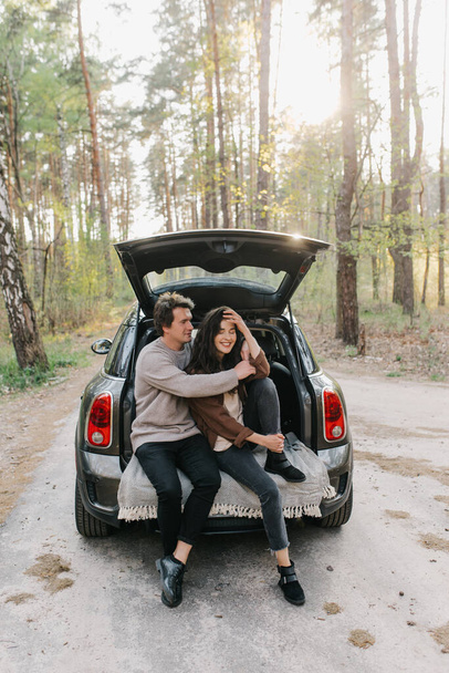 Young beautiful couple relaxing together sitting on a car trunk - Photo, image