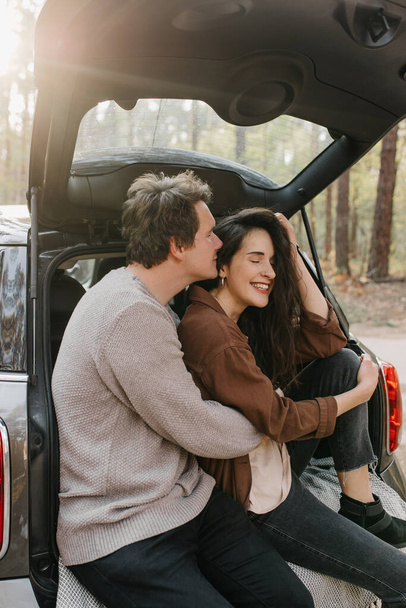 Young beautiful couple relaxing together sitting on a car trunk - Foto, imagen