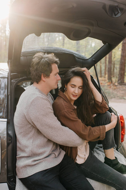 Young beautiful couple relaxing together sitting on a car trunk - Foto, Imagem