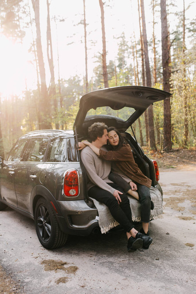 Young beautiful couple relaxing together sitting on a car trunk - Zdjęcie, obraz