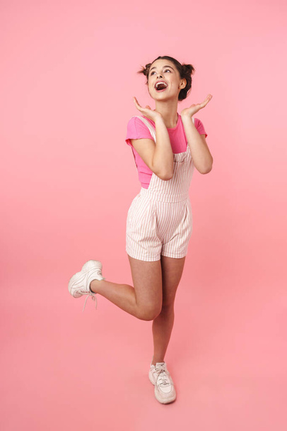 Full length of a pretty young teenage girl jumping isolated over pink background, rejoycing - Foto, Imagem
