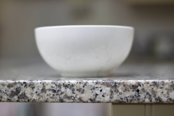 Tigela de cerâmica branca em pé no topo de trabalho granito manchado cinza
 - Foto, Imagem