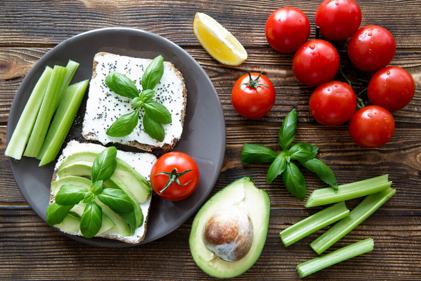 Tasty healthy snack, avocado sandwiches with fresh celery and cherry tomatoes on brown table background.  - Foto, Bild
