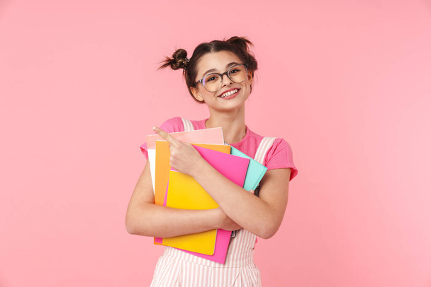 Happy teenage girl standing isolated over pink background, carrying textbooks - Valokuva, kuva