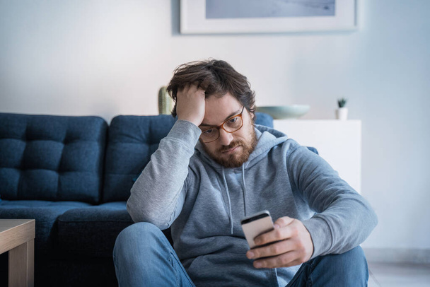Portrait of worried guy holding cellphone at home - Φωτογραφία, εικόνα