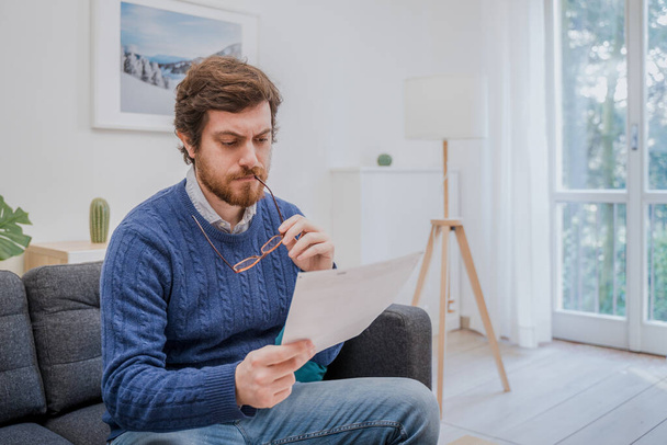 Mies lukee negatiivisia uutisia kirjeessä kotona sohvalla - Valokuva, kuva