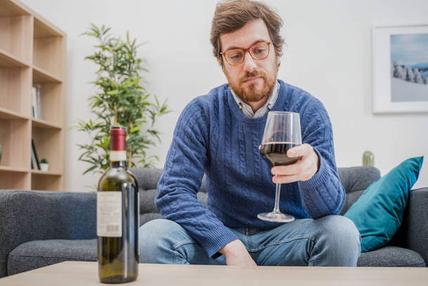 Ritratto di uomo con bevanda alcolica seduto sul divano di casa - Foto, immagini