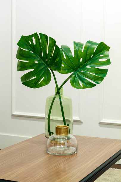 monstera leaves in a glass vase on a wooden table in an elegant interior - Fotografie, Obrázek