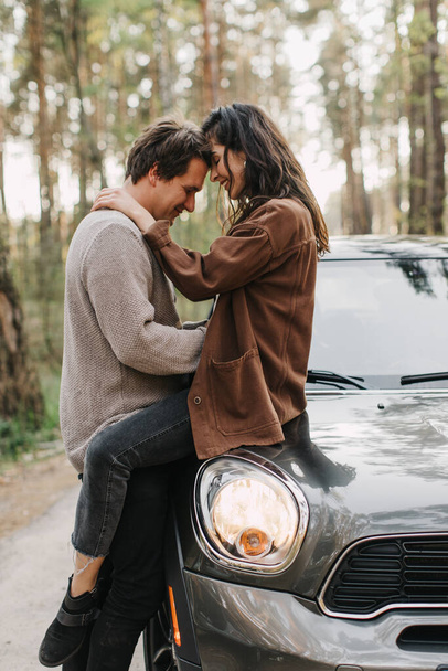 beautiful young couple in love kisses and hugs sitting on a car - Foto, immagini