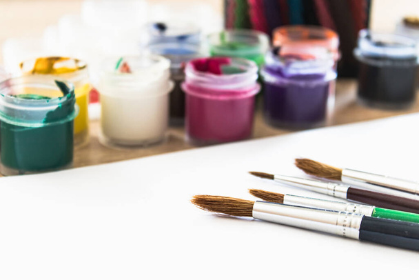 Auf dem Tisch liegen mehrfarbige Gouache im Glas und Pinsel zum Malen. Set für Zeichnen, Kreativität und Hobbys. Nahaufnahme. - Foto, Bild