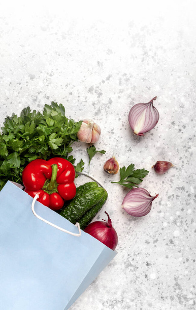 Eco friendly. Zero waste. Paper package blue craft with vegetables Bulgarian red pepper, cucumbers, garlic, onions, parsley, greens on a concrete background with copy space. Flat lay. Stop plastics - Photo, Image