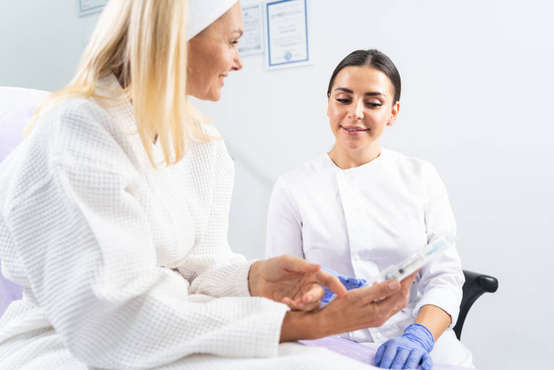 Dermatologist looking at a cosmetic product in her patients hand - Foto, afbeelding