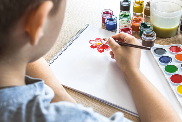 The child draws gouache on a white sheet and jars of paint are on the table. Hobbies and entertainment for children. Close-up. - Photo, Image
