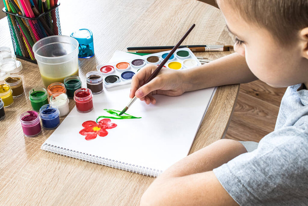 El niño dibuja gouache en una sábana blanca y frascos de pintura están sobre la mesa. Pasatiempos y entretenimiento para niños. Primer plano
. - Foto, imagen