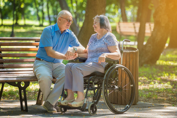 Homme âgé parlant avec une femme en fauteuil roulant à l'extérieur dans un parc d'été
. - Photo, image