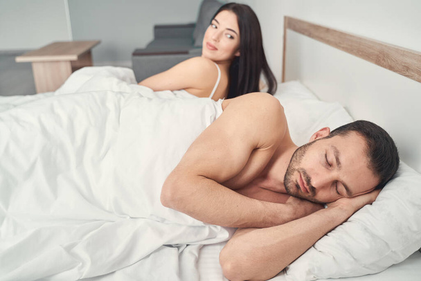 Woman lying in bed next to a sleeping man - Valokuva, kuva
