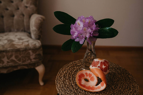 Rododendron in vaas en grapefruit op de rieten stoel - Foto, afbeelding