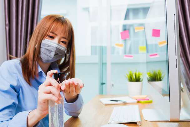 Asian young business woman wearing face mask protective working from home office with laptop computer he quarantines disease coronavirus or COVID-19 and cleaning hands with sanitizer alcohol gel pump - Fotoğraf, Görsel