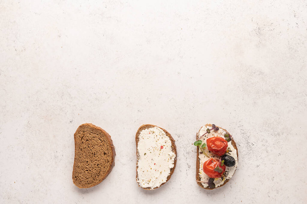 Stages of making a sandwich of bread, ricotta cheese, salted salmon, baked tomatoes and greens on light background - 写真・画像