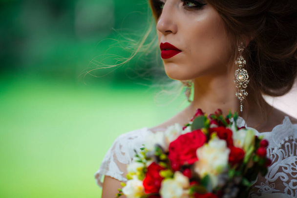 Beautiful bride with a wedding bouquet in her hands outdoors in the park. - Fotografie, Obrázek