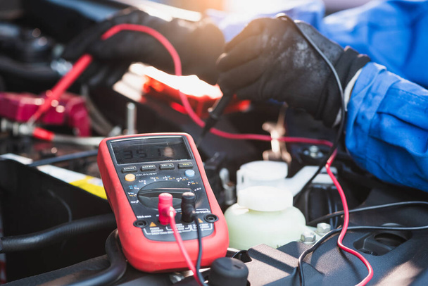 La imagen abstracta del técnico que utiliza el voltímetro para medir el voltaje de la batería de un coche. el concepto de automoción, reparación, mecánica, vehículo y tecnología
. - Foto, imagen