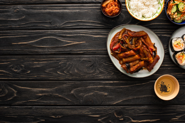 vista superior de kimchi coreano, kimbap e topokki perto de arroz e óleo de gergelim na superfície de madeira
 - Foto, Imagem
