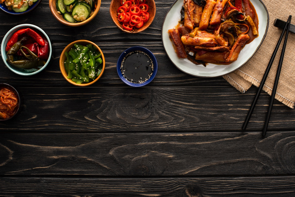 bovenaanzicht van Koreaanse topokki bij eetstokjes, lekkere bijgerechten en katoenen servet op houten ondergrond  - Foto, afbeelding