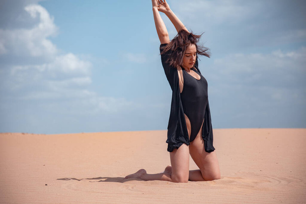 A girl in a black swimsuit sits on the sand in the desert - Fotografie, Obrázek