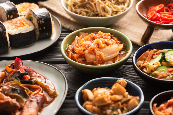 selective focus of traditional spicy kimchi and topokki near tasty korean dishes on wooden surface  - Foto, immagini