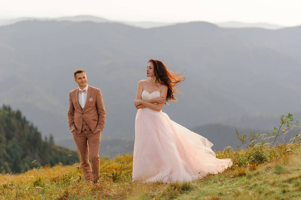 The bride and groom are standing close to each other against the backdrop of autumn mountains. The groom admires his wife. - Photo, Image