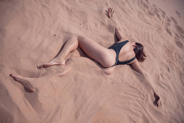 The girl in a black piece swimsuit lies on the sand in the desert - Foto, Imagen