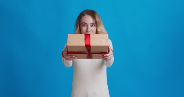 Cheerful young woman offering gift box to camera and smiling - Video