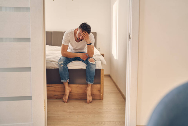 Sad male sitting on this bed with his head on his hand - Foto, Bild